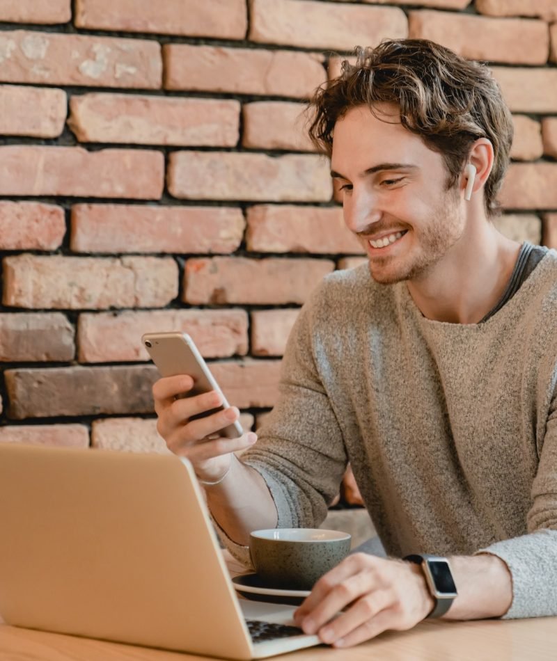 25s smiling attractive businessman working on his laptop and phone in loft cafeteria