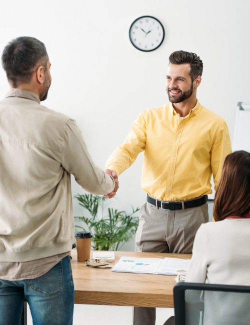 advisor and investor shaking hands over table wile woman sitting in office