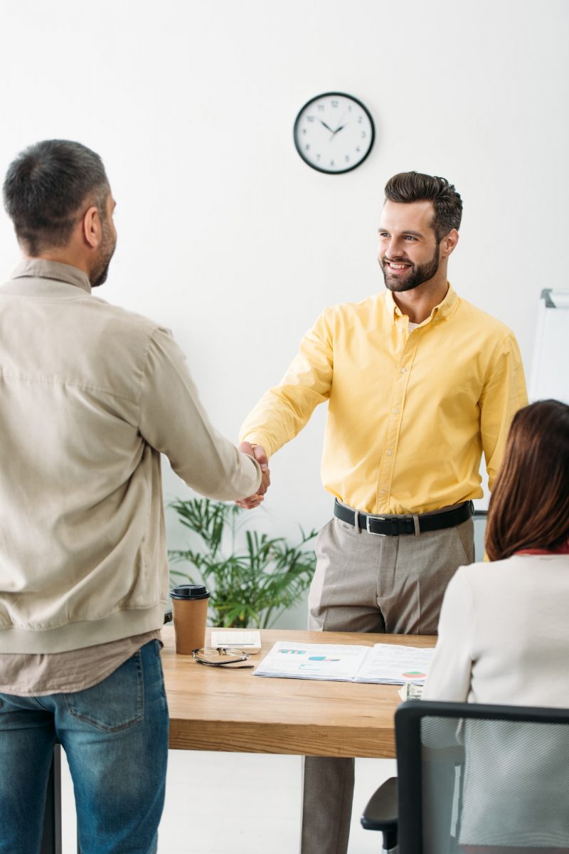 advisor and investor shaking hands over table wile woman sitting in office