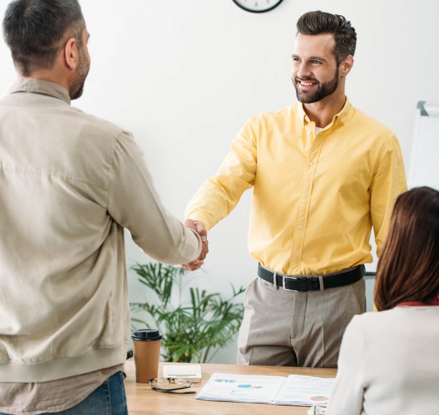 advisor and investor shaking hands over table wile woman sitting in office