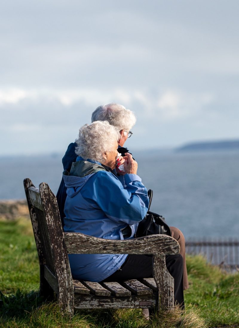Old woman and man sitting on a bench near the sea
